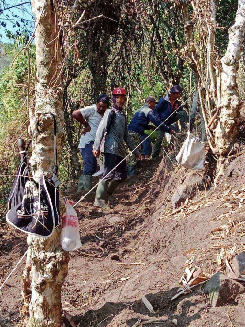 Puluhan warga Dusun Bendorejo, Desa Sumberagung, Ngantang, bekerja bakti membuka jalur pendakian di lereng Puncak Srege. Mereka membawa cangkul dan sekop, dengan latar belakang perbukitan hijau dan Waduk Selorejo yang terlihat di kejauhan.